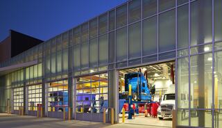 A modern garage with large glass doors showcases two trucks being serviced, illuminated in soft evening light.