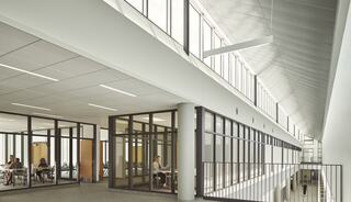 A bright, modern interior features large windows and glass-partitioned rooms, promoting an open and collaborative workspace.