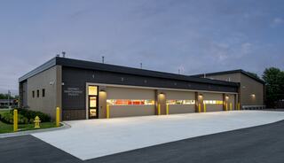 A modern maintenance facility features a sleek design, large garage doors, and a clear, well-maintained parking area under evening skies.