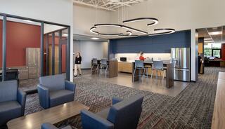 A modern, spacious workspace featuring a kitchenette, seating area, and stylish lighting, designed for collaboration and relaxation.