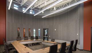 A modern conference room features a large, oval table surrounded by ergonomic chairs, with a curved wall and natural lighting.
