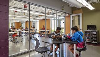 Students work at tables in a modern classroom, collaborating on projects and engaging in hands-on activities while others focus individually.