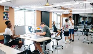 A modern classroom filled with students engaged in various activities, some working at desks while others interact and collaborate.