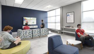 A modern gaming lounge features students playing video games on a big screen, relaxing on stylish furniture with a cozy atmosphere.