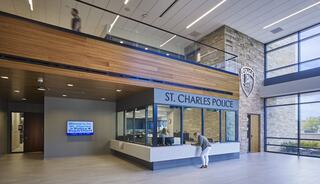 A modern police station interior with large windows, wood accents, and a reception area. Officers assist visitors in a bright, open space.
