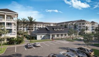 A modern apartment complex featuring multiple buildings, lush landscaping, and a parking area under a clear blue sky.