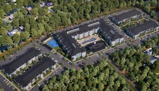 Aerial view of a modern residential complex surrounded by trees, featuring multiple buildings, a pool, and ample parking spaces.