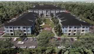 Aerial view of a residential complex surrounded by greenery, featuring multiple buildings, parking spaces, and a landscaped courtyard.