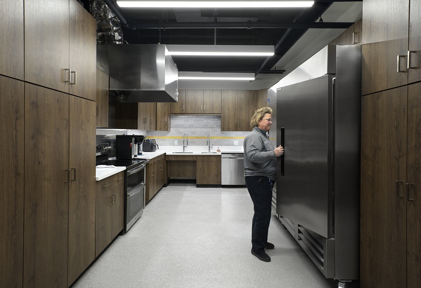 A modern kitchen features sleek cabinetry and appliances, with a person opening a large stainless steel refrigerator. Soft lighting enhances the space.