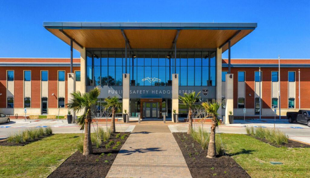 A modern public safety headquarters featuring a glass facade, lush landscaping, and a welcoming entrance with palm trees.