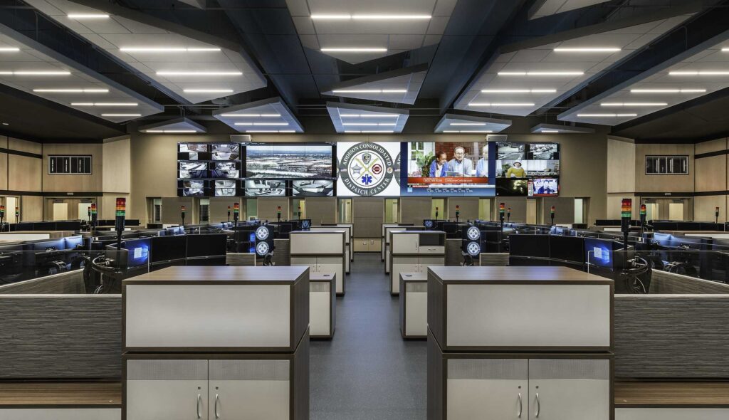 A modern command center features rows of workstations, large screens displaying information, and a sleek, organized interior design.