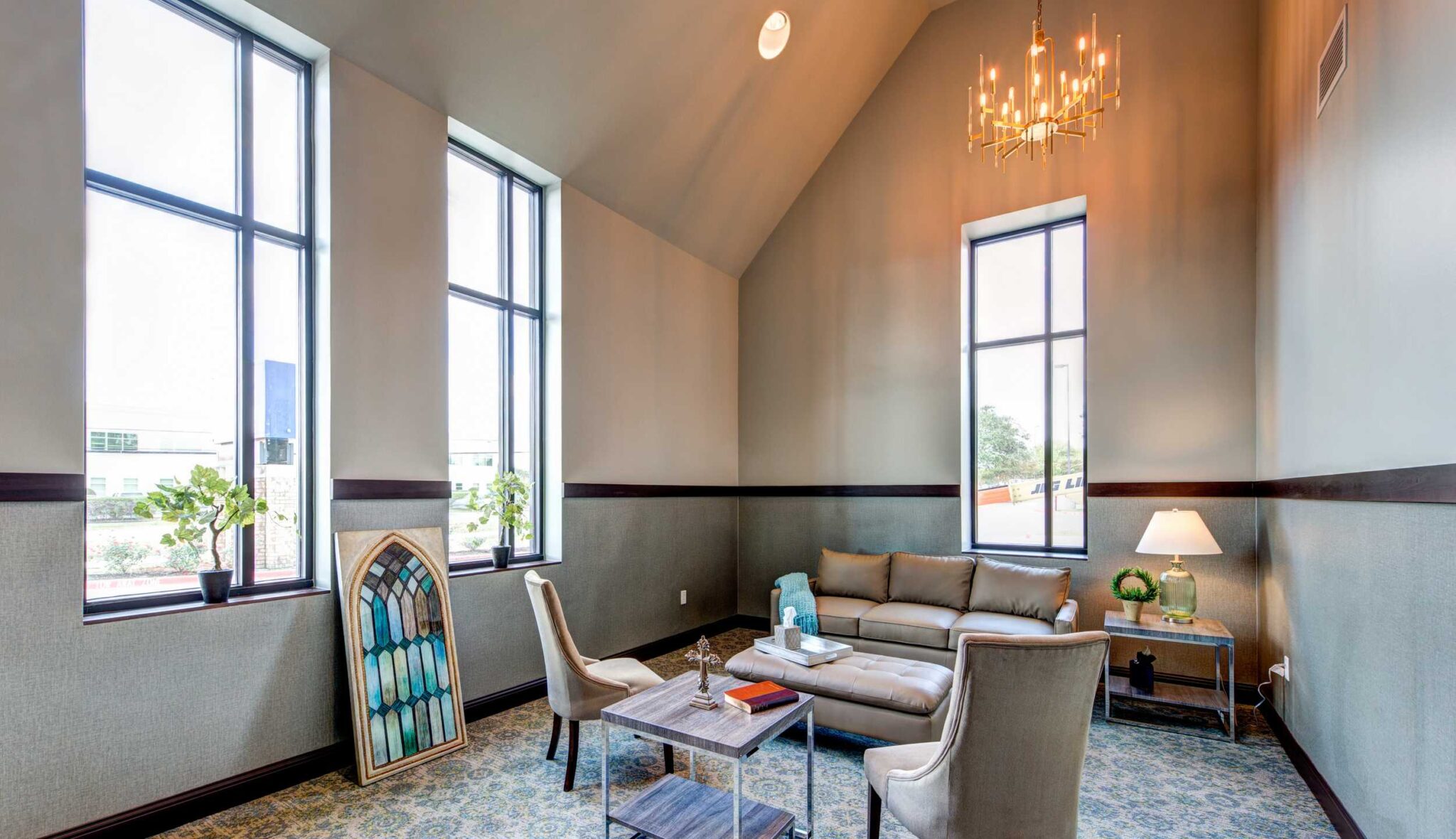 A fitness room features various workout equipment, including weights, a treadmill, and a large window overlooking a patio.