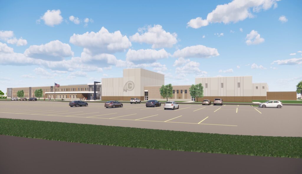 A modern school building with a spacious parking lot, surrounded by greenery under a clear blue sky, featuring clouds in the background.