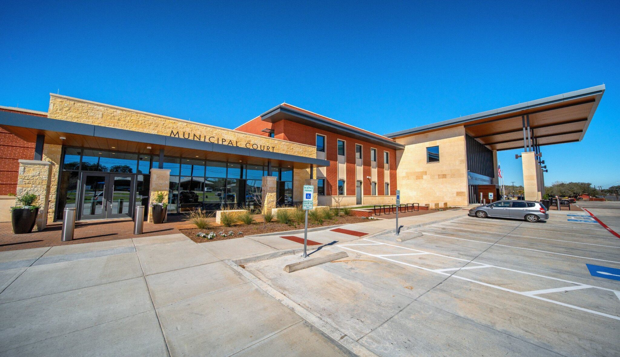 Modern municipal court building featuring a sleek design, large glass windows, and a spacious parking area under a clear blue sky.