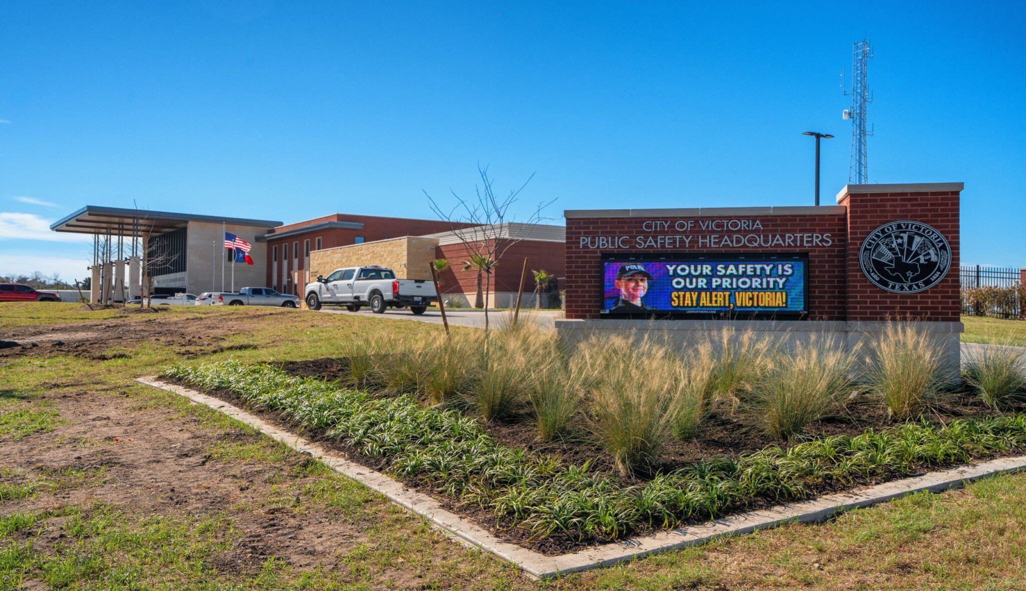 Public safety headquarters in Victoria features a modern building, signage prioritizing safety, and a landscaped entrance with flags.