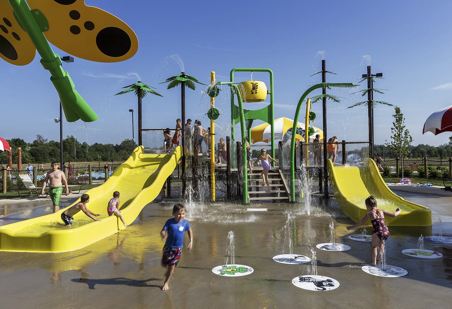 Children enjoy a vibrant water play area with slides, splash features, and playful decorations under a clear blue sky. Fun and laughter abound!