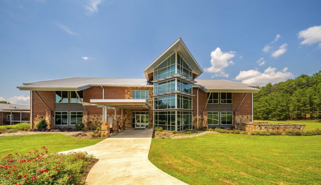 A modern worship center with a mix of brick and glass features, surrounded by green grass and landscaping under a clear blue sky.