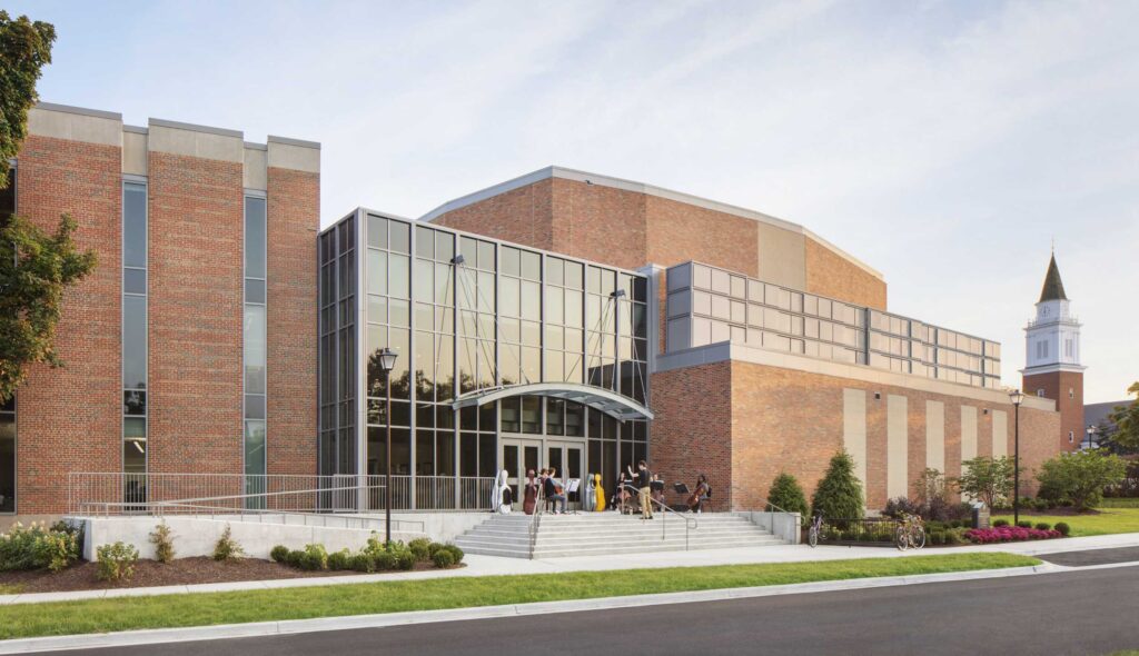 A modern brick building features large glass windows, an inviting entrance, and manicured landscaping, surrounded by a peaceful setting.