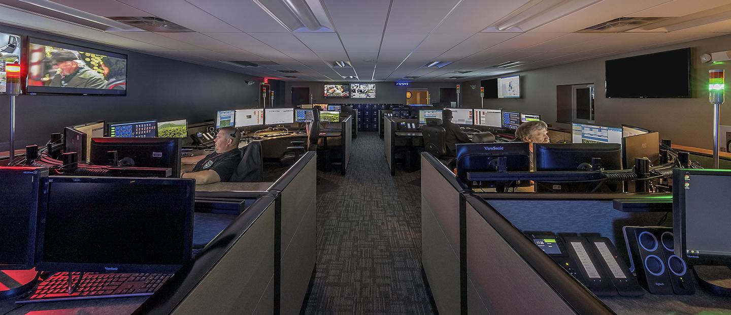 A spacious control room with multiple workstations, monitors, and dim lighting, showcasing staff engaged in various tasks.