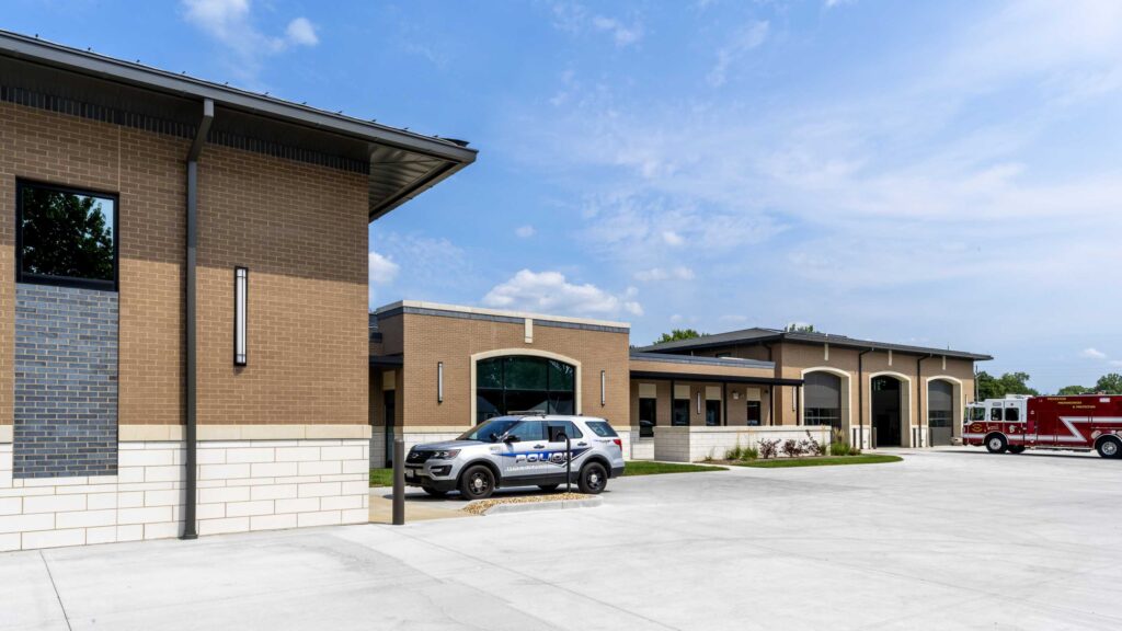 A modern building complex featuring a police vehicle outside, with another structure nearby and clear blue skies above.