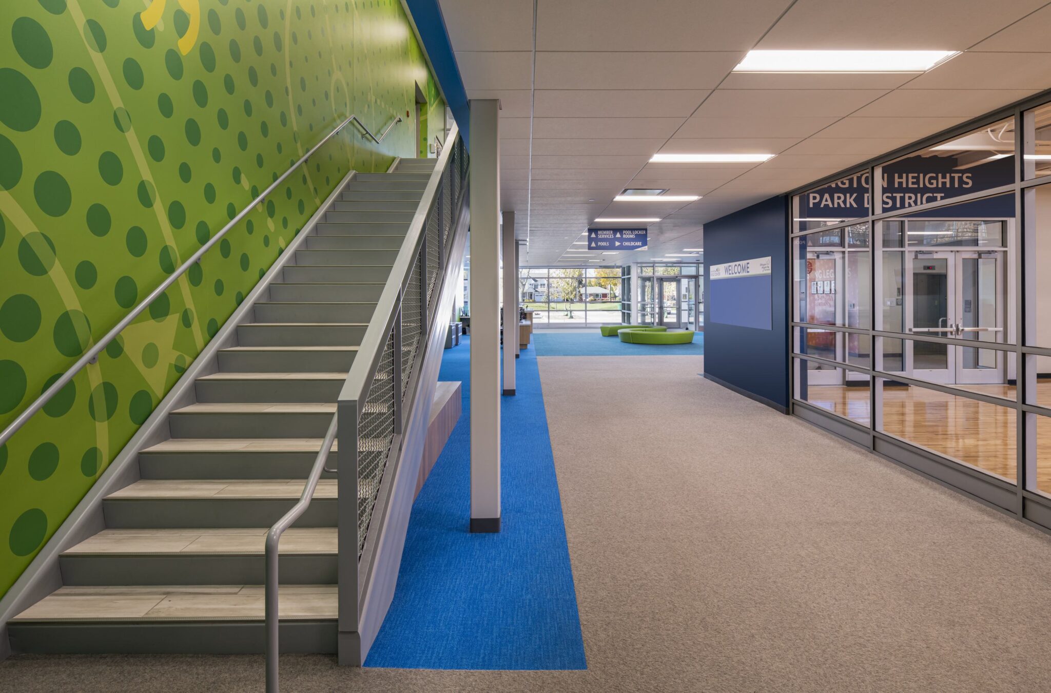 A spacious, modern interior features a staircase, colorful wall designs, and a mix of carpet and flooring, creating an inviting atmosphere.