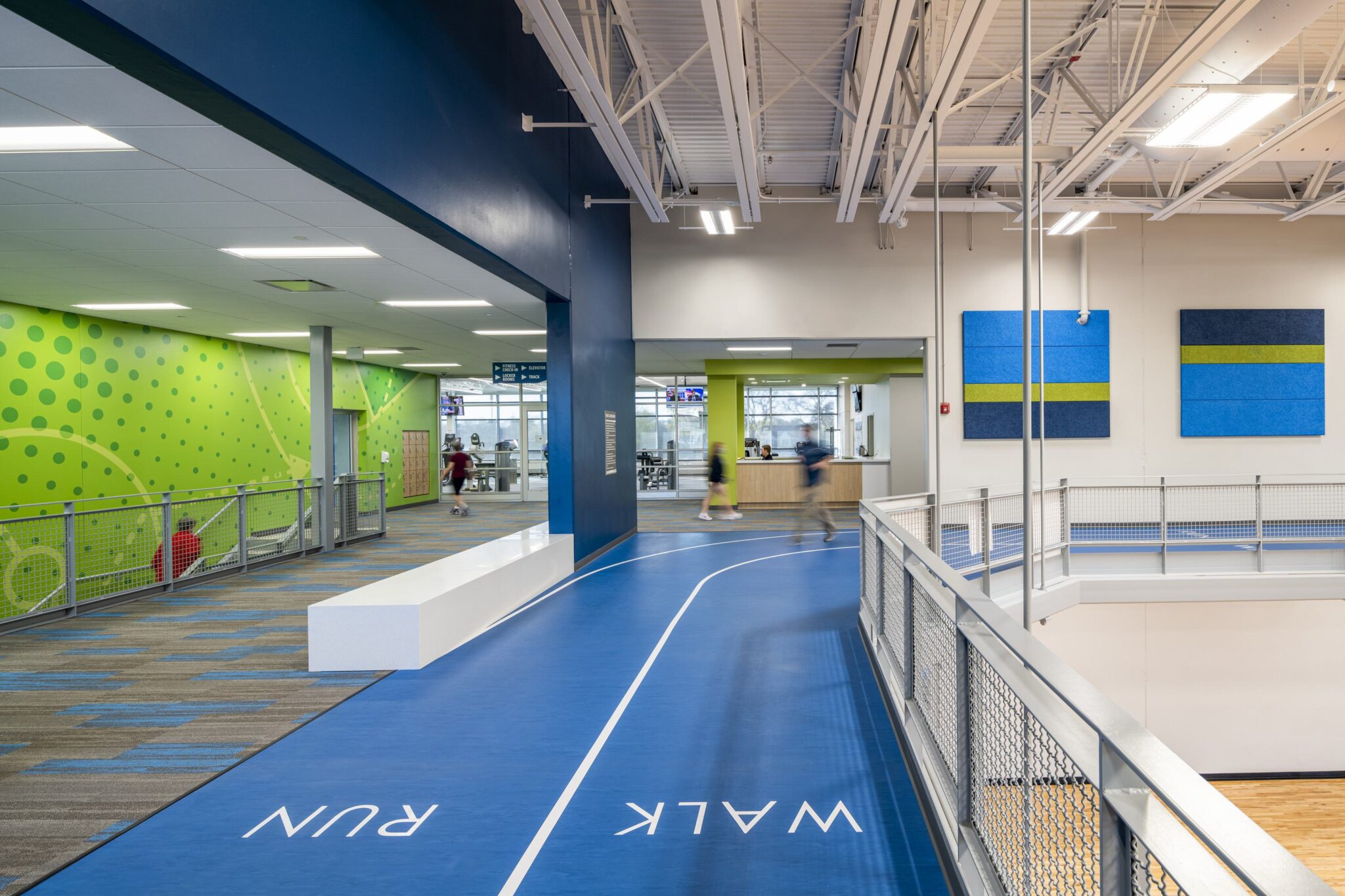 A spacious indoor track with clearly marked "WALK" and "RUN" sections, surrounded by vibrant green and blue walls, bustling with activity.