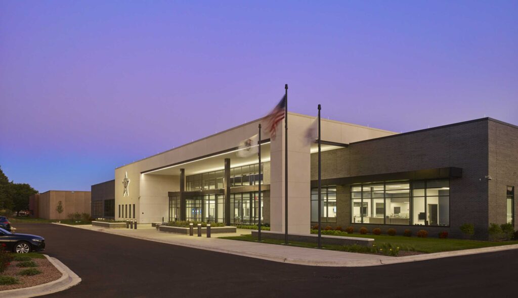 A modern building features sleek architecture, large glass windows, and flags, set against a twilight sky. A clean parking area complements it.