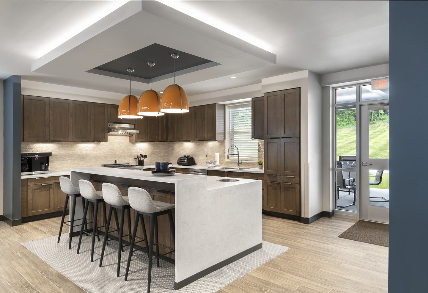 A modern kitchen features a large island with seating, dark wood cabinets, elegant lighting, and a welcoming atmosphere leading to an outdoor space.