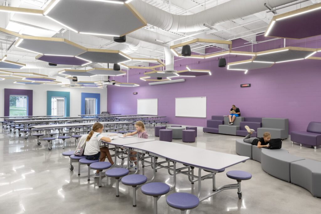 A modern classroom features flexible seating with students engaged in various activities, bright natural light, and interactive learning spaces.