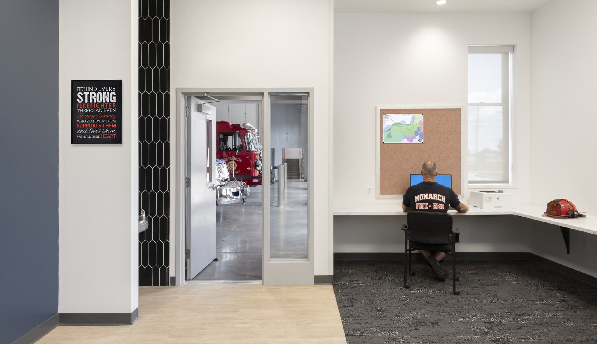 A modern workspace features a man at a desk, with a doorway leading to a fire truck visible in the background. Inspirational wall art is present.