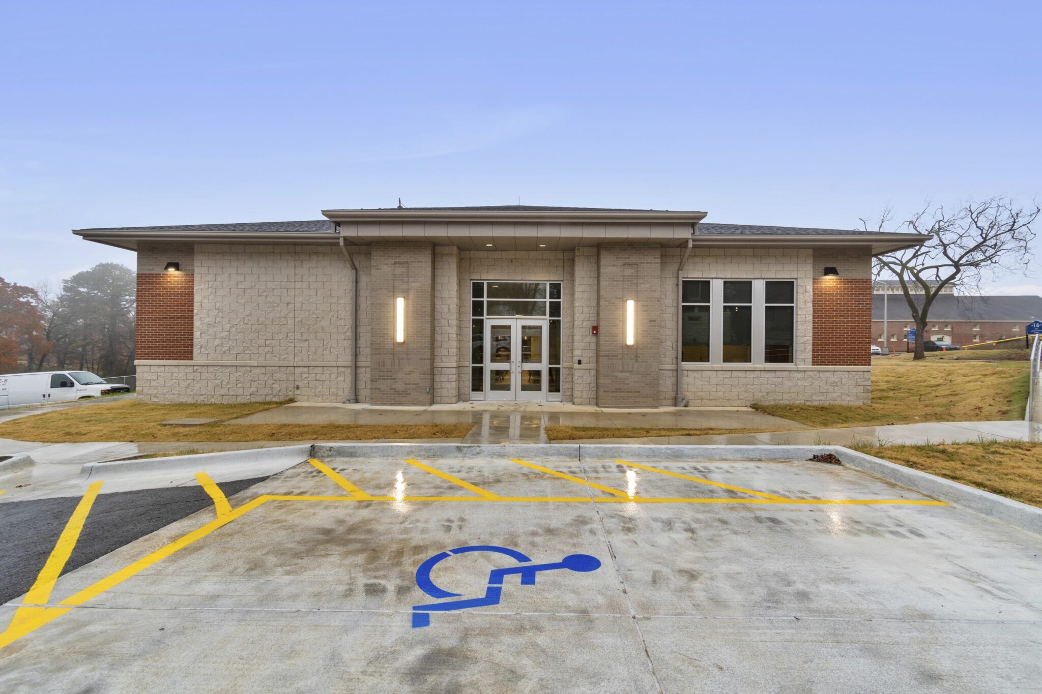 A modern building with a light-colored stone facade, large windows, and accessible parking, set against a clear sky.