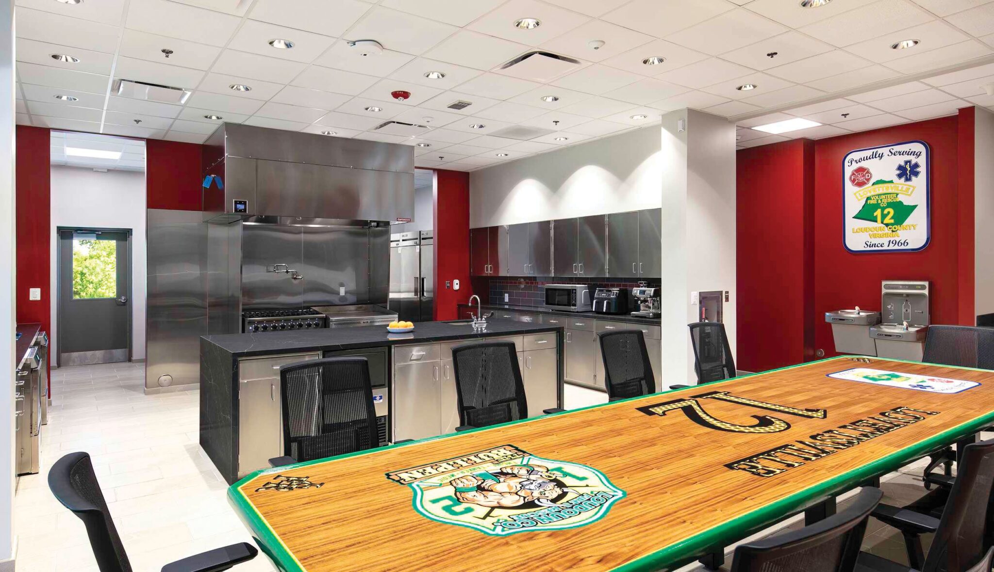 Modern fire station kitchen with stainless steel appliances, an inviting dining table, and vibrant red walls. Ideal for communal gatherings.