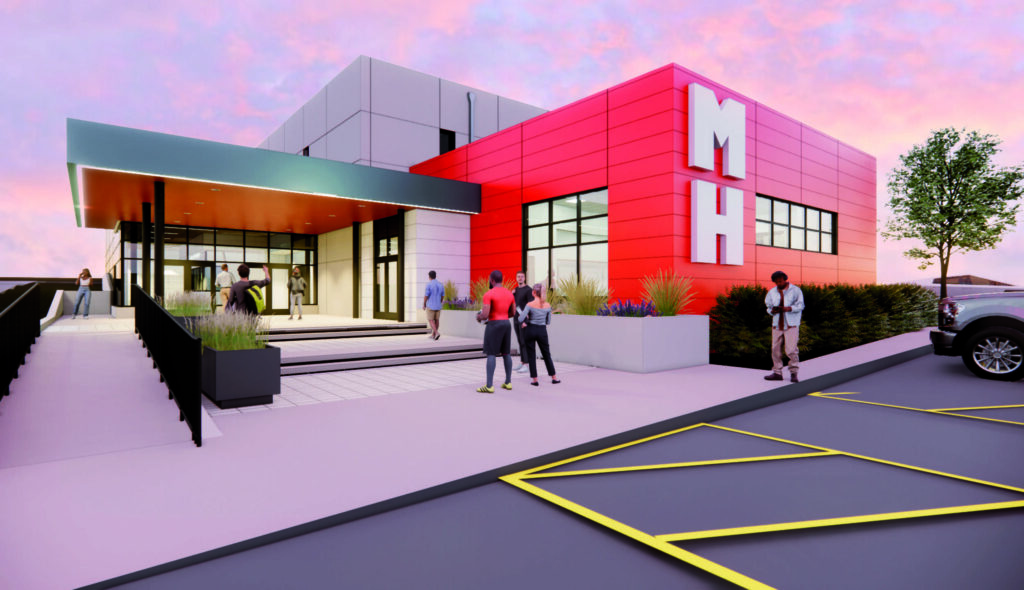 A modern, colorful building with large windows, a welcoming entrance, and landscaped surroundings, featuring the initials "MH" prominently.