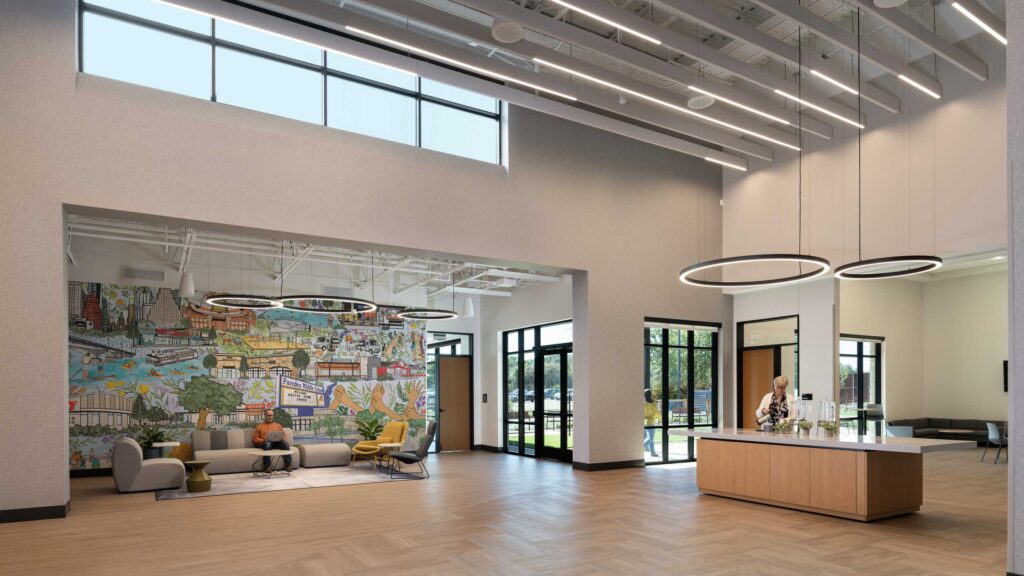 A spacious lobby features a welcoming reception area and a vibrant mural, complemented by modern furnishings and abundant natural light.