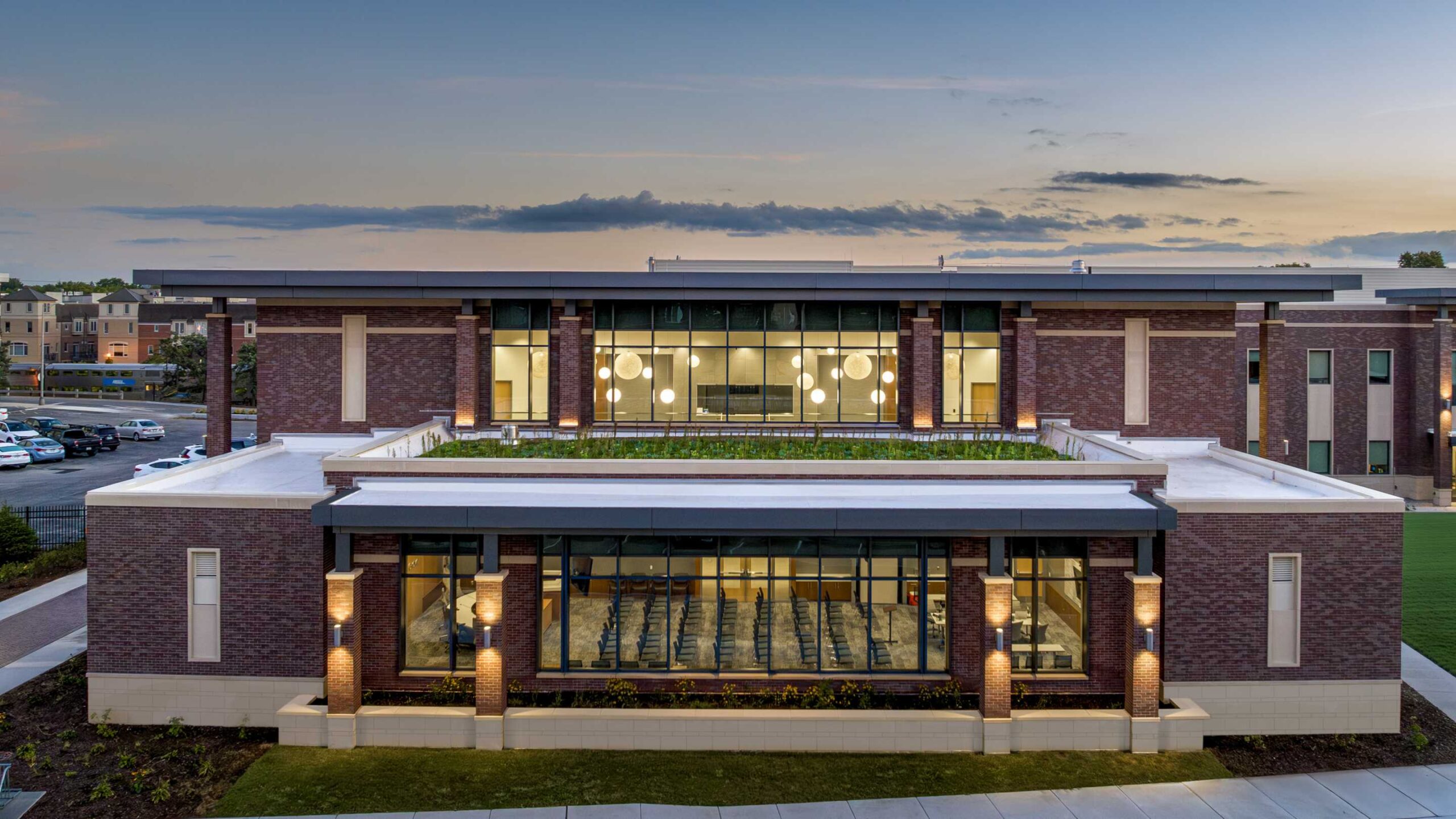 A modern brick building features large windows, an inviting entrance, and a spacious rooftop area, surrounded by landscaped greenery.