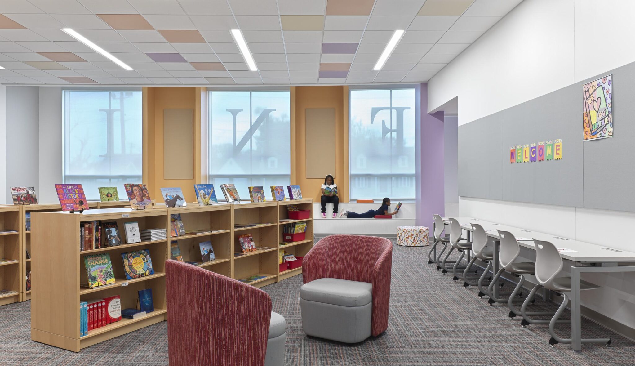 A bright, modern library space features bookshelves, cozy seating areas, and study tables, creating an inviting atmosphere for reading and learning.