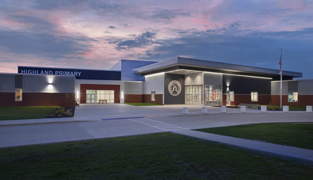 A modern school building with a large entrance, featuring a sign that reads "Highland Primary," against a twilight sky.