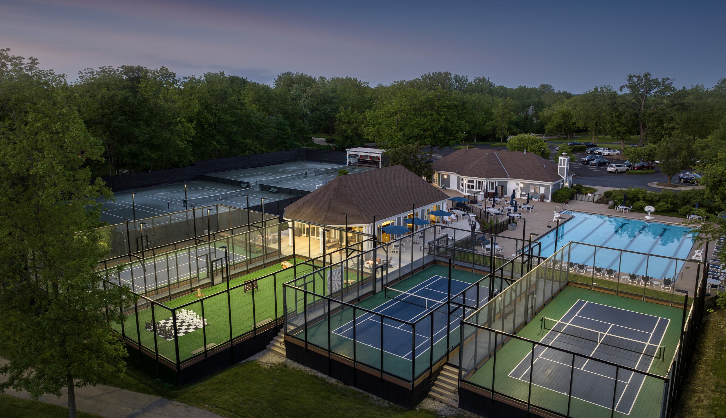 A vibrant recreational complex features tennis courts, paddle tennis, a swimming pool, and an inviting clubhouse, surrounded by lush greenery.