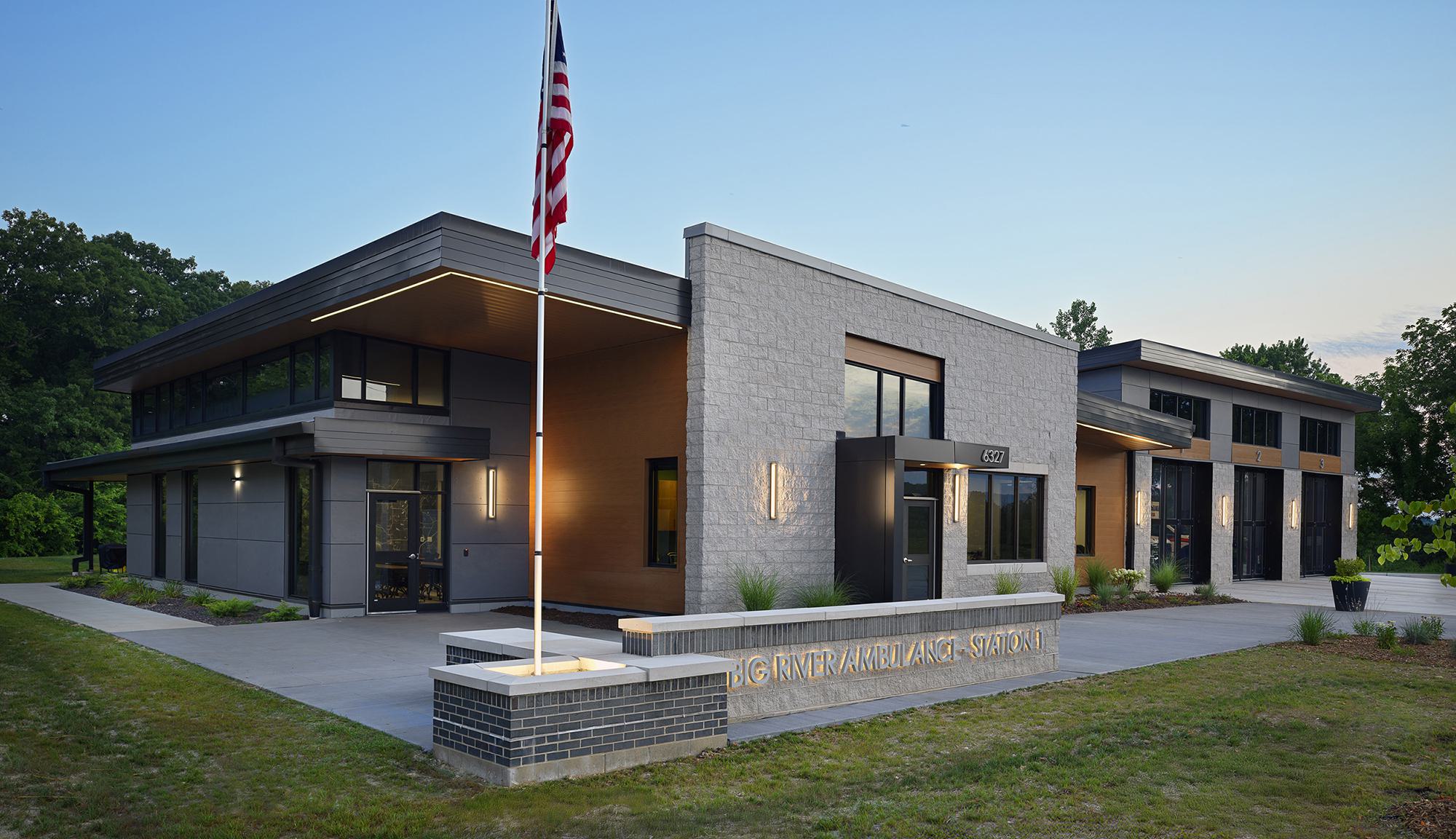 A modern building featuring a mix of brick and metal design, with large windows and an American flag prominently displayed in front.