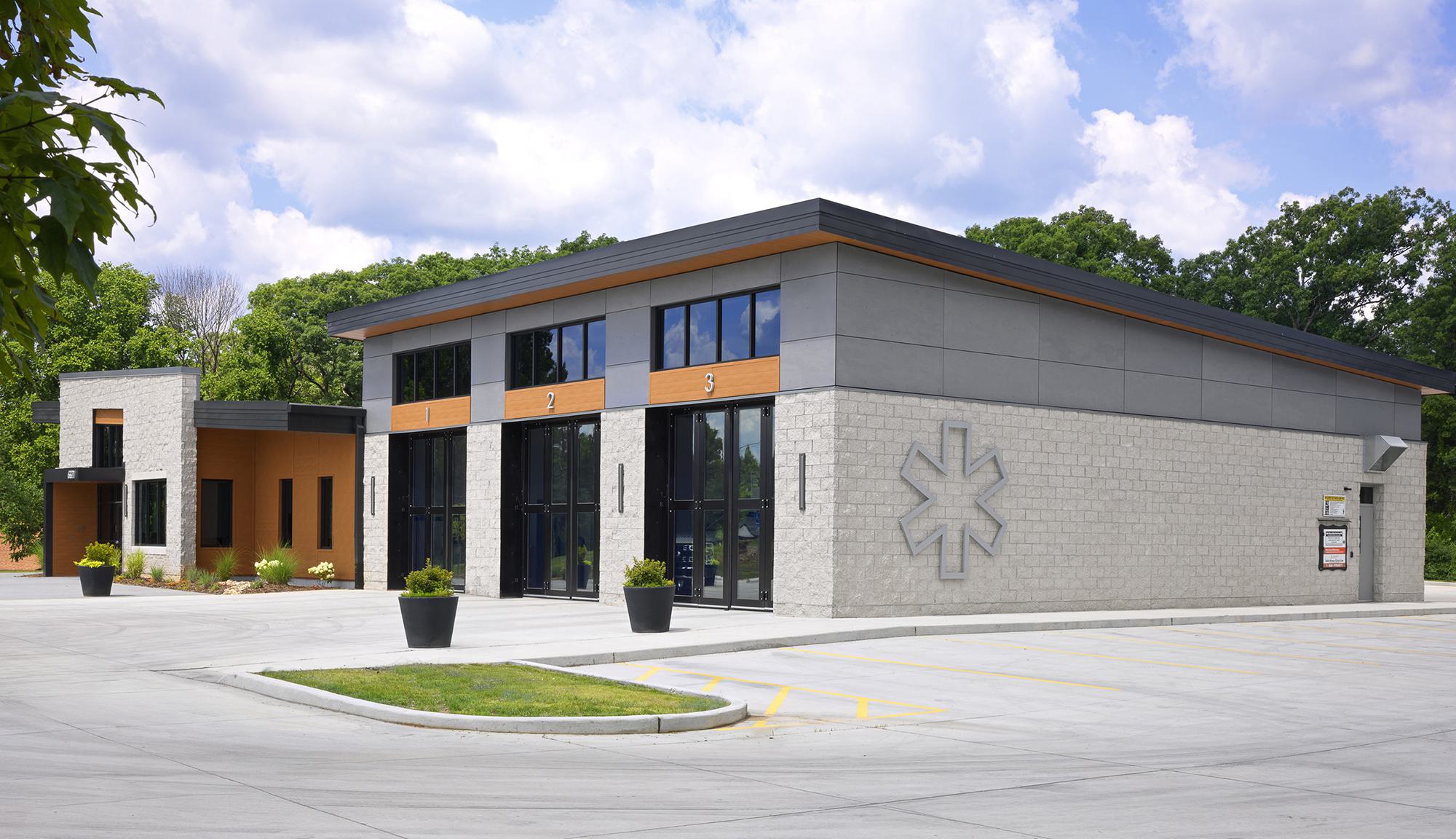 A modern, two-tone building with large glass windows, featuring an asterisk logo, surrounded by a landscaped area and a spacious parking lot.