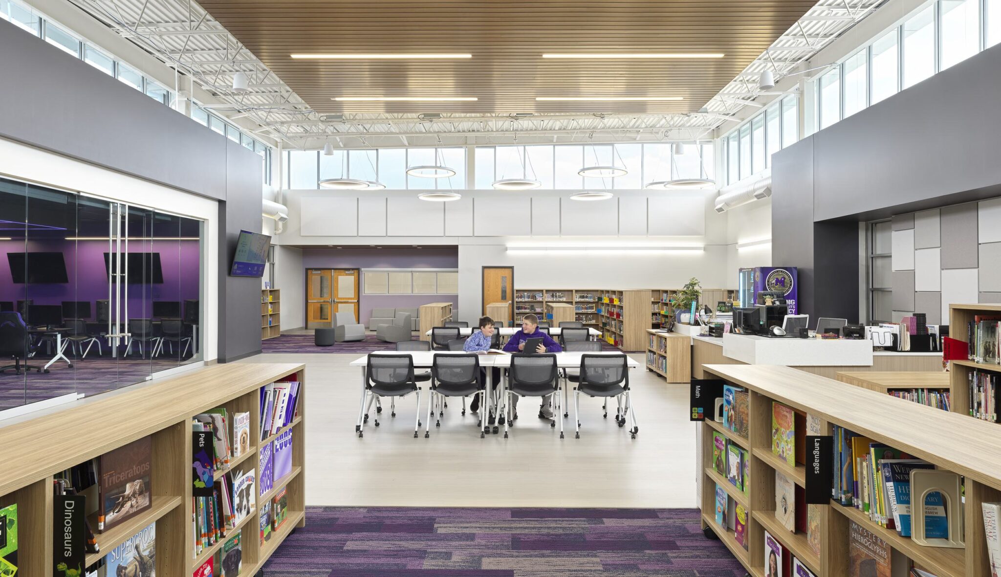 A spacious, modern library featuring vibrant decor, large windows, bookshelves, and a collaborative workspace with students working together.