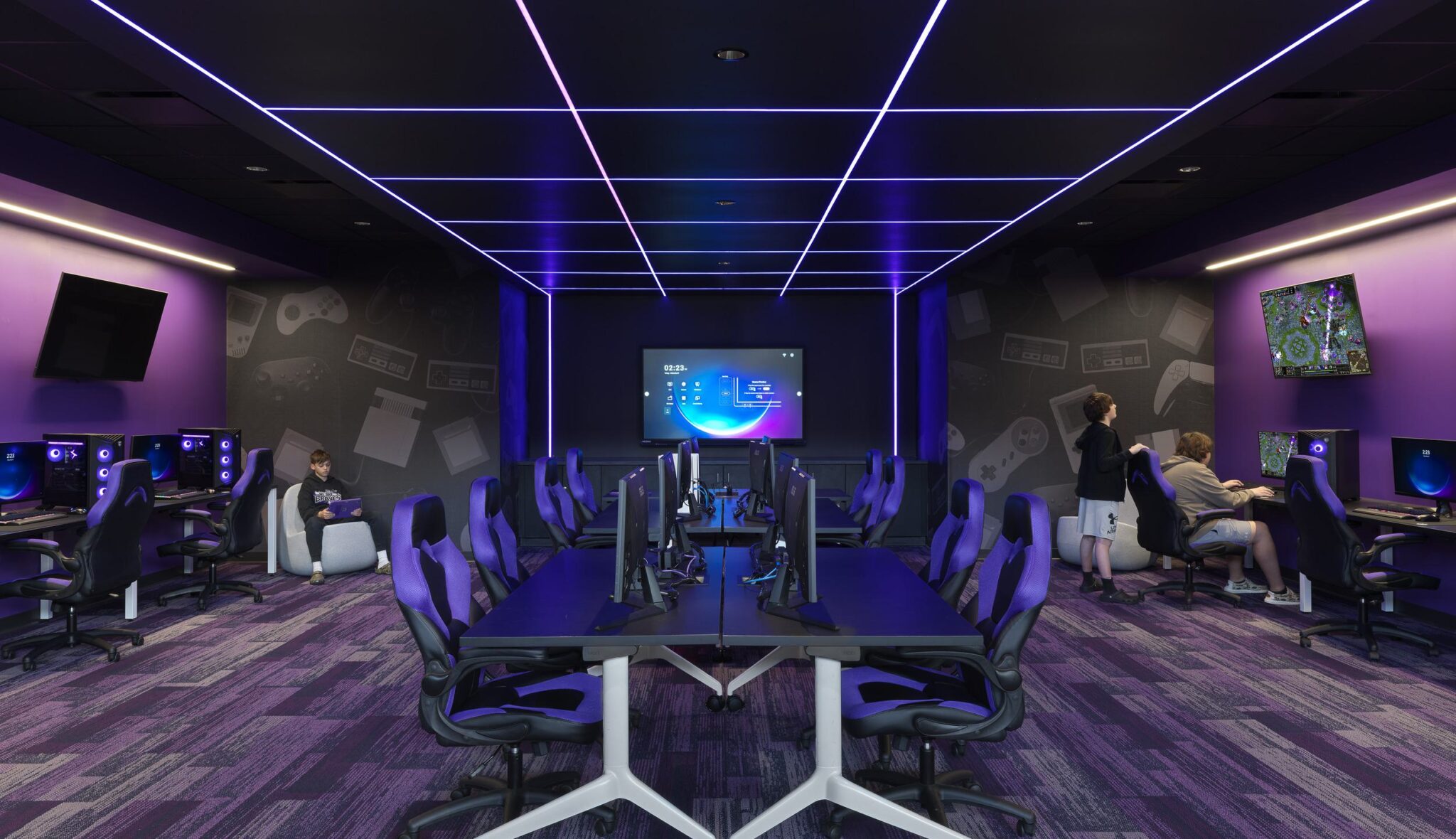 A gaming room featuring sleek purple decor, multiple workstations with high-end chairs, and large screens for immersive digital experiences.