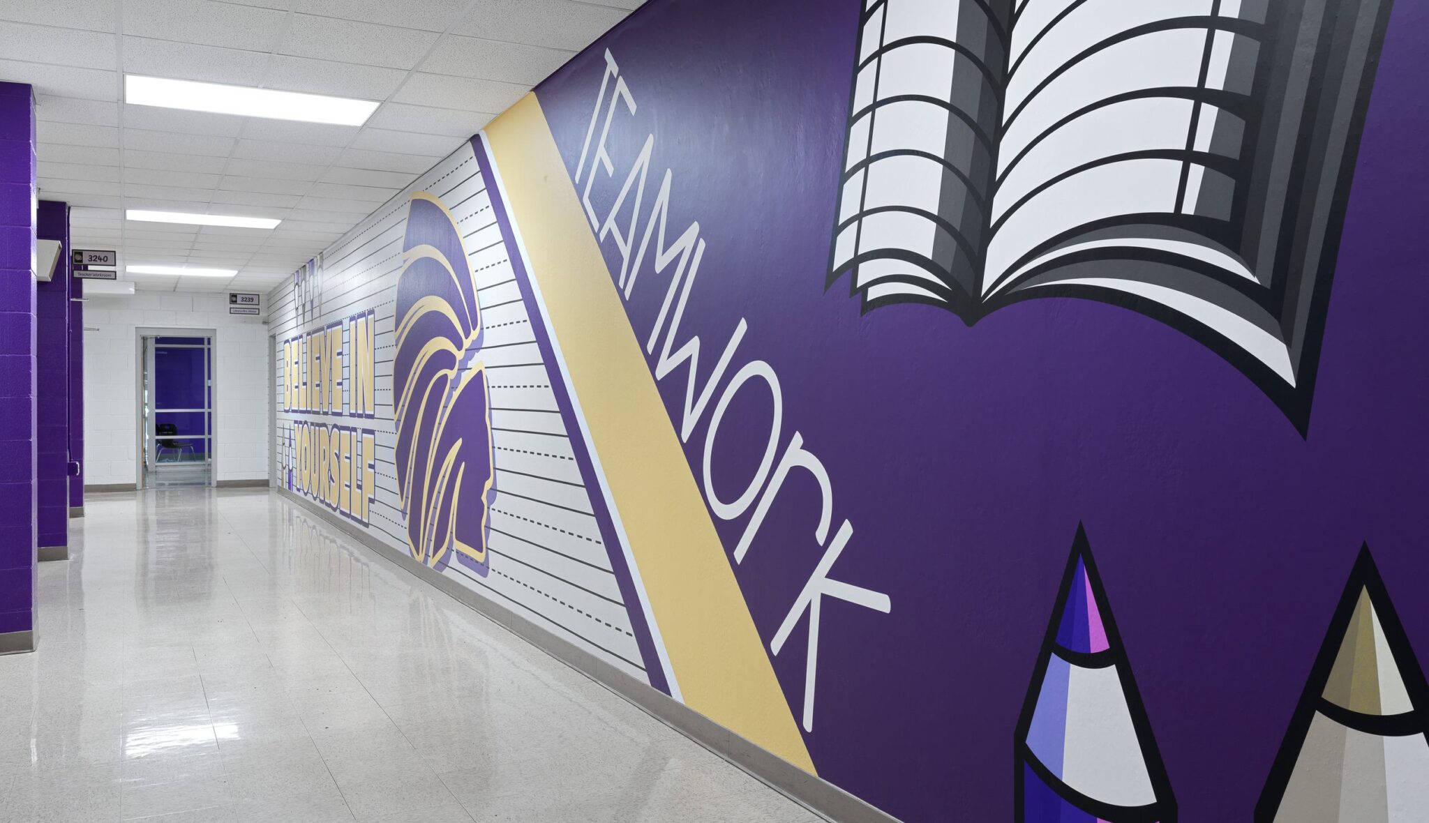 A vibrant hallway features a mural emphasizing "TEAMWORK," alongside colorful illustrations of a book and educational themes.