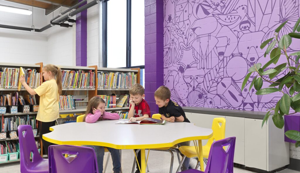 A colorful library scene features children reading at a round table, while another child browses books in a vibrant, engaging environment.