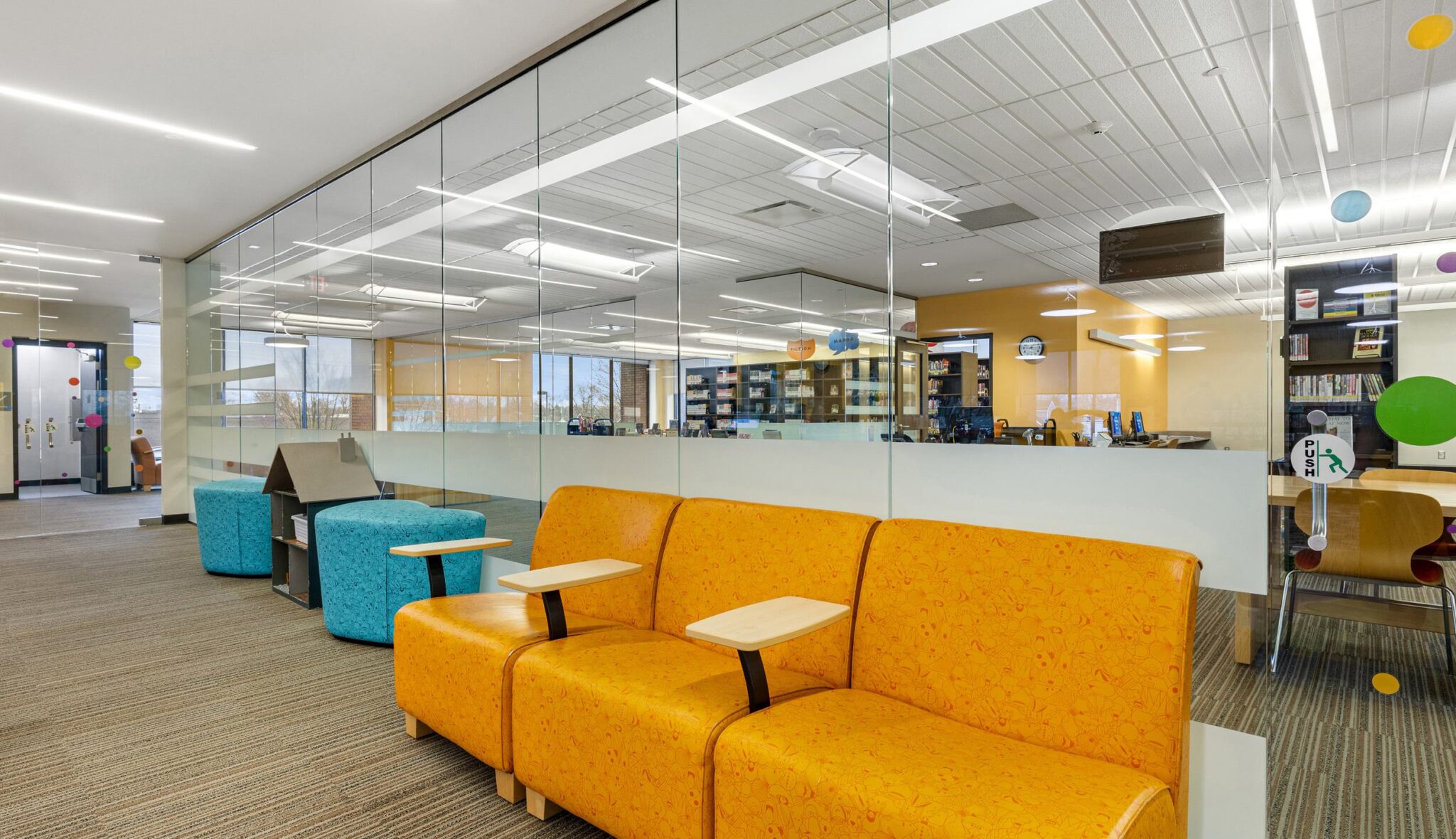 A modern library space features bright orange and blue seating, glass walls, and colorful decor, encouraging collaboration and learning.