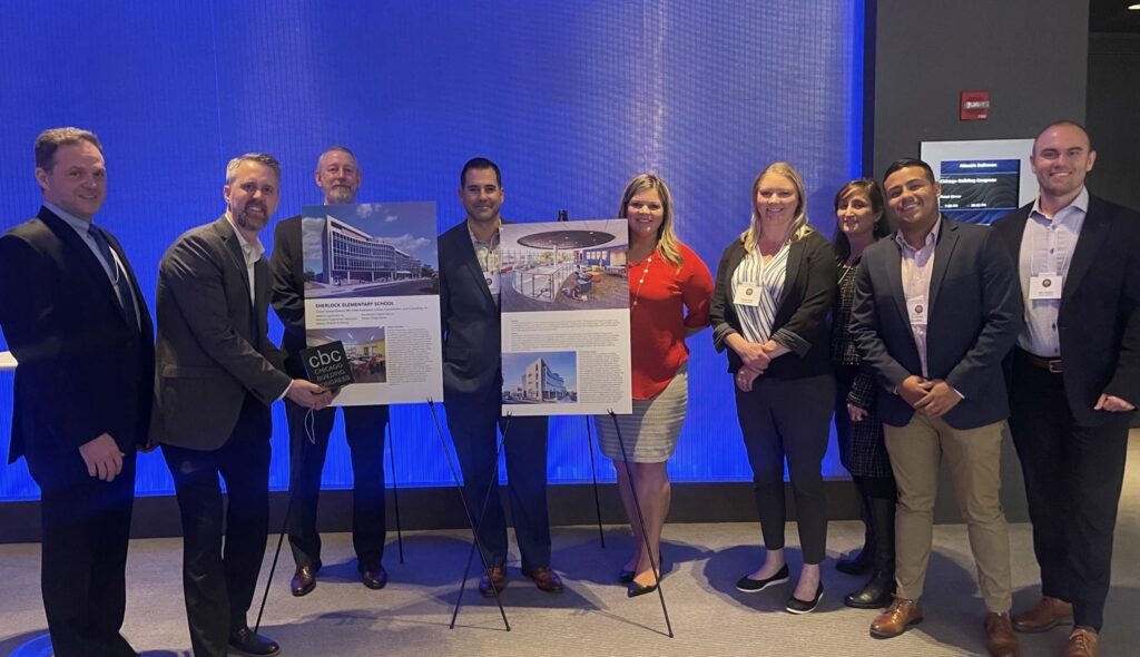 A group of professionals poses with project presentations on display boards, showcasing architectural designs in a modern event setting.