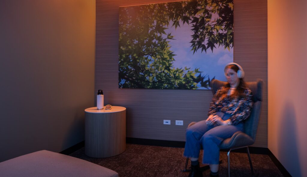 A person sits in a cozy room with soft lighting, wearing headphones, as a nature-themed artwork adorns the wall behind them.