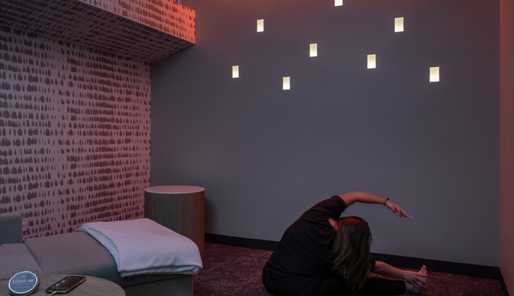 A person practices stretching or yoga in a softly lit, modern room with unique wall fixtures, creating a calming atmosphere.