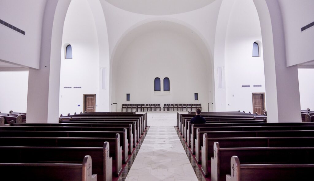 A spacious, modern interior of a church features long wooden pews, arched ceilings, and subtle lighting, creating a serene atmosphere.