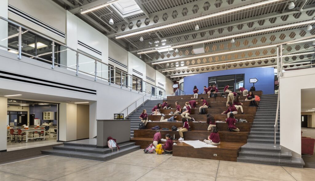 A spacious, contemporary educational space features tiered seating, where students engage in activities, fostering collaboration and learning.